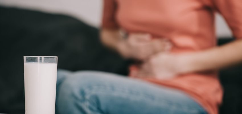 cropped view of woman with lactose intolerance holding stomach near glass of milk