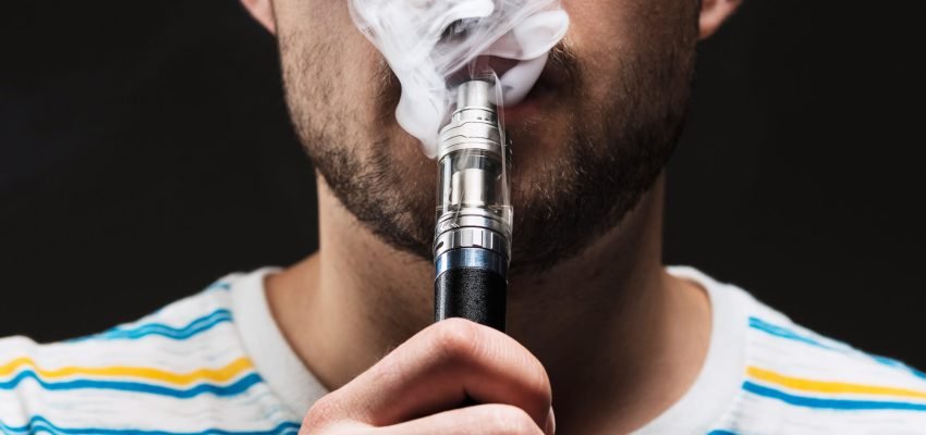 The face of vaping young man on black studio background